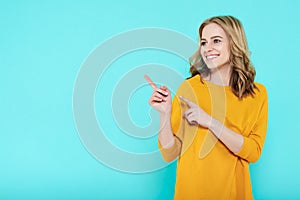 Trendy attractive young woman wearing casual clothes posing over pastel blue background. Smiling woman pointing with both hands.