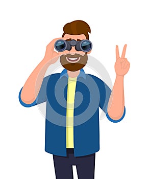 Trendy bearded man in casual wear looking through binoculars and gesturing, making victory, V, peace or number two sign with hand.