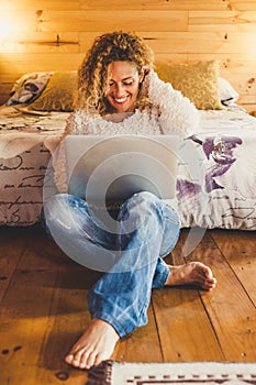 Trendy beautiful cheerful happy woman sitting on the wooden floor at home or hotel with modern laptop computer internet connected