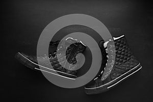 Trendy black quilted sneakers walking on blackboard background. Minimalist black, dark mode, fasion shoes concept. Flat lay, copy