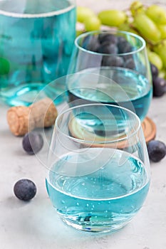 Trendy blue moscato wine in glass and in bottle, green and red grape on background, vertical