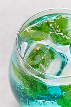 Trendy blue moscato wine in glass, served with mint ice cubes, vertical, closeup