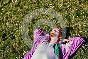 Trendy caucasian man lying in the field of green grass with copy space with his eyes closed