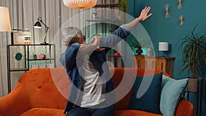 Trendy cheerful mature old man dancing and moving to rhythm making dub dance gesture at modern home