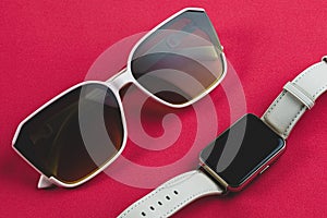 trendy composition of sunglasses and smart watch on a red background