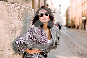 Trendy fashion woman in jacket and sunglasses walking on the street, urban city scene. Copy space