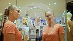 Trendy girl looks in mirror and try outfits in modern shopping centre department store.Happy shopper girl posing in