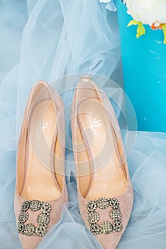 Trendy, graceful suede high heel shoes and wedding rings and jewelery in a blue suede chair. Wedding details.