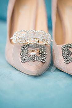 Trendy, graceful suede high heel shoes and wedding rings and jewelery in a blue suede chair. Wedding details.