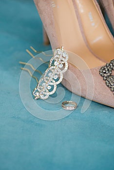 Trendy, graceful suede high heel shoes and wedding rings and jewelery in a blue suede chair. Wedding details.