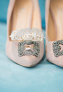 Trendy, graceful suede high heel shoes and wedding rings and jewelery in a blue suede chair. Wedding details.