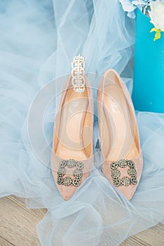 Trendy, graceful suede high heel shoes and wedding rings and jewelery in a blue suede chair. Wedding details.