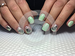 Trendy green manicure with a stylish design and black leaf