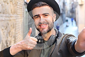 Trendy handsome man taking a selfie and giving a thumbs up outdoors