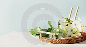 Trendy and healthy summer infused vitamin water with cucumber, mint and blueberry in wicker tray on blue sky background