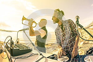 Trendy hipster dj playing summer hits at sunset beach party