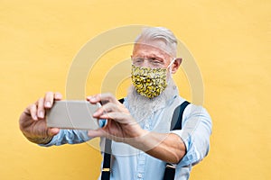 Trendy hipster man using mobile phone doing video call while wearing fashion silk safety mask - Outfit, technology and lifestyle