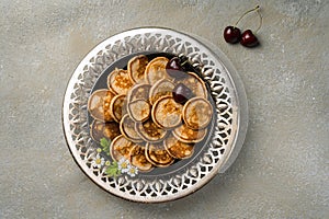 A trendy homemade breakfast with tiny pancakes close-up. Mini pancakes, cherries, tea on the table in an openwork plate