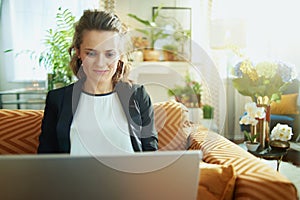 Trendy housewife writing on laptop while sitting on sofa