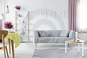 Interior design with comfortable scandinavian couch, wooden coffee table, striped rug and graphics on the floor, real photo