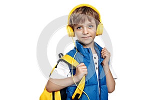 Trendy little boy wearing headphone and yellow backpack looking to camera on white background. Back to School.