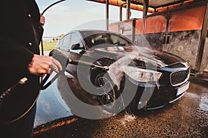 Trendy man in jeans and blaser is washing his own car at car washing station.