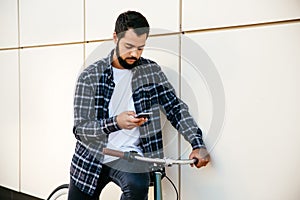Trendy man using a smartphone while sitting on bike, outside