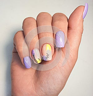 Trendy manicure with purple and yellow flowers. Women`s manicure with pastel violet and yellow and black twigs.