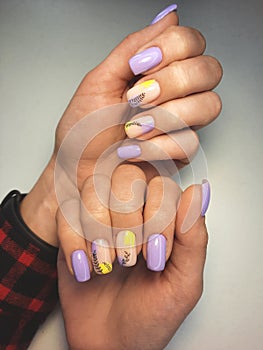 Trendy manicure with purple and yellow flowers. Women`s manicure with pastel violet and yellow and black twigs.