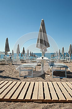 Trendy mediterranean beach with sun umbrellas and sunbeds with blue sea and blue sky on background. Perfect summer