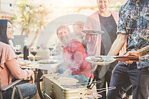 Trendy man cooking and serving meat at barbecue dinner outdoor - Chef grilling food for family friends at bbq meal outside -