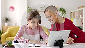 Trendy mid adult woman helping her daughter doing school homework at home