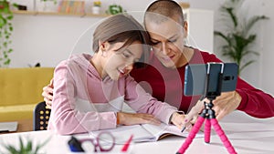 Trendy mid adult woman helping her daughter doing school homework at home