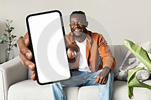 Trendy mobile phone. Happy black man holding smartphone with white empty screen, showing device to camera, mock up