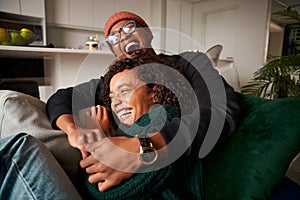 Trendy multi-ethnic adult couple sitting on sofa laughing hysterically. High quality photo