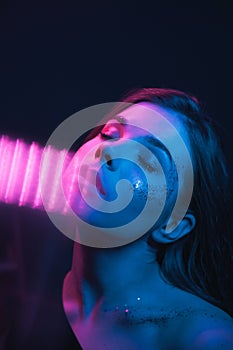 Trendy night portrait of a woman with bright makeup in purple and blue light, posing for the camera with her eyes closed. Vertical