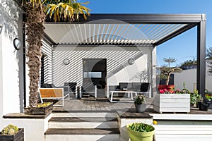 Trendy outdoor patio pergola. garden lounge, chairs, metal grill surrounded by landscaping