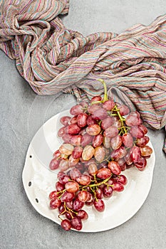 Trendy plate with a bunch of pink grapes. Vintage textile napkin, stone concrete background