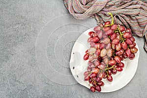 Trendy plate with a bunch of pink grapes. Vintage textile napkin, stone concrete background