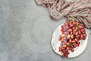 Trendy plate with a bunch of pink grapes. Vintage textile napkin, stone concrete background