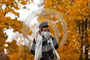 Trendy positive young woman model in fashionable warm clothes in a vintage hat with a scarf enjoys a walk in the park on a October