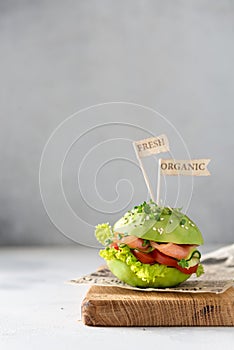 Trendy Raw Vegan avocado burger with fesh vegetables and salted salmon on wooden board on gray background. Side view. Restaurant photo