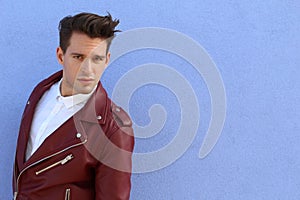 Trendy relaxed young man with a modern haircut standing against a blue background looking at the camera, three quarter pose