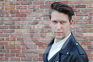 Trendy relaxed young man with a modern haircut standing against a blue background looking at the camera, three quarter pose