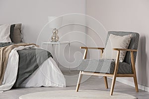 Trendy retro armchair with pillow in spacious bedroom interior with king size bed and lamp on bedside table