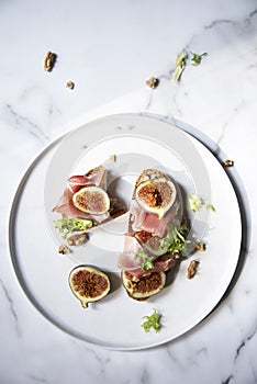 Trendy sandwiches with ham and figs on white plate and white marble patterned backgorund.