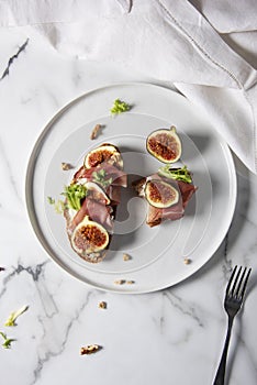 Trendy sandwiches with ham and figs on white plate and white marble patterned backgorund.