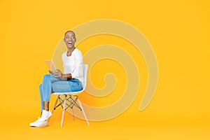 Trendy smiling African American woman sitting on a chair using tablet computer