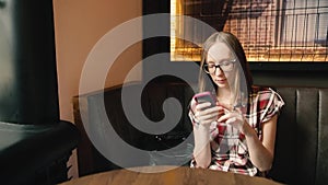 Trendy smiling girl in glasses chatting in social networks or reading something.