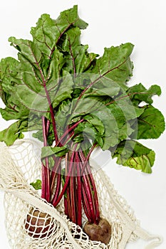 Trendy string bag with fresh young beetroot and haulm over light white background